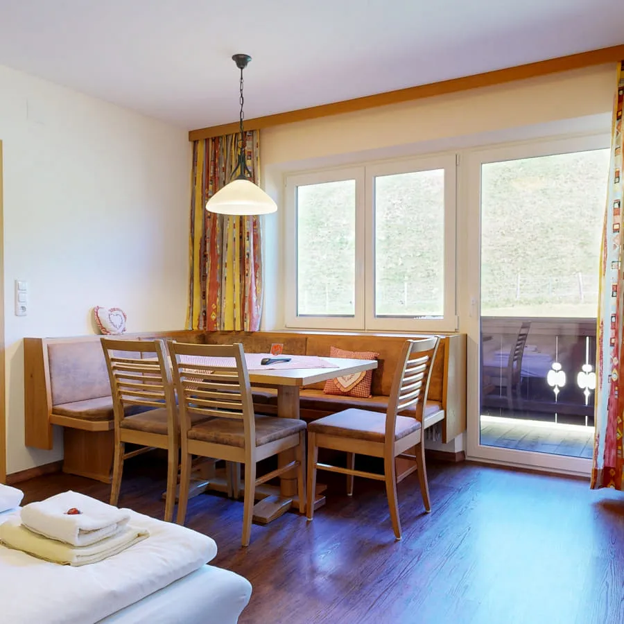 Innenansicht einer Unterkunft mit Esstisch, Sesseln und Zugang zu einem Balkon.