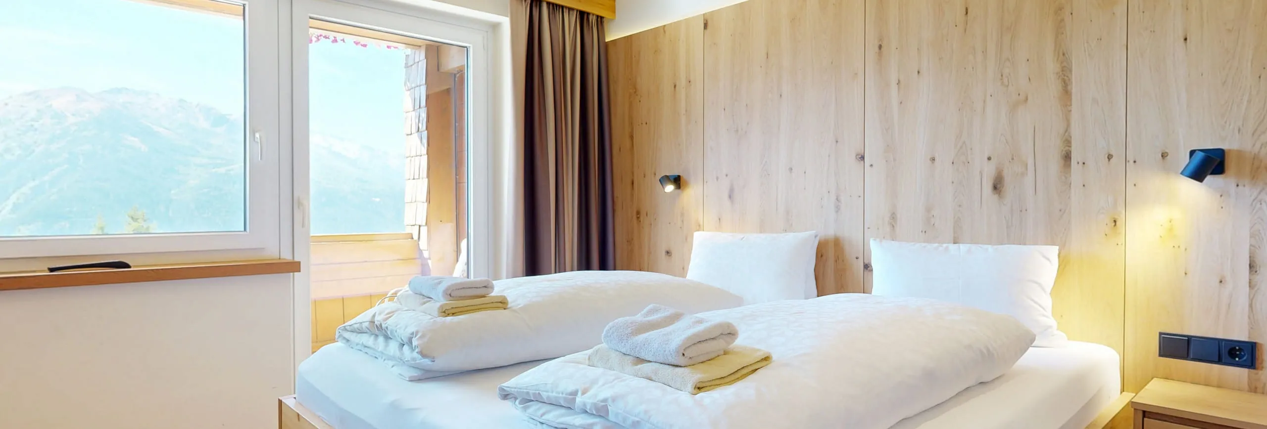 Helles Schlafzimmer mit Holzverkleidung und Blick auf Berge durch das Fenster.