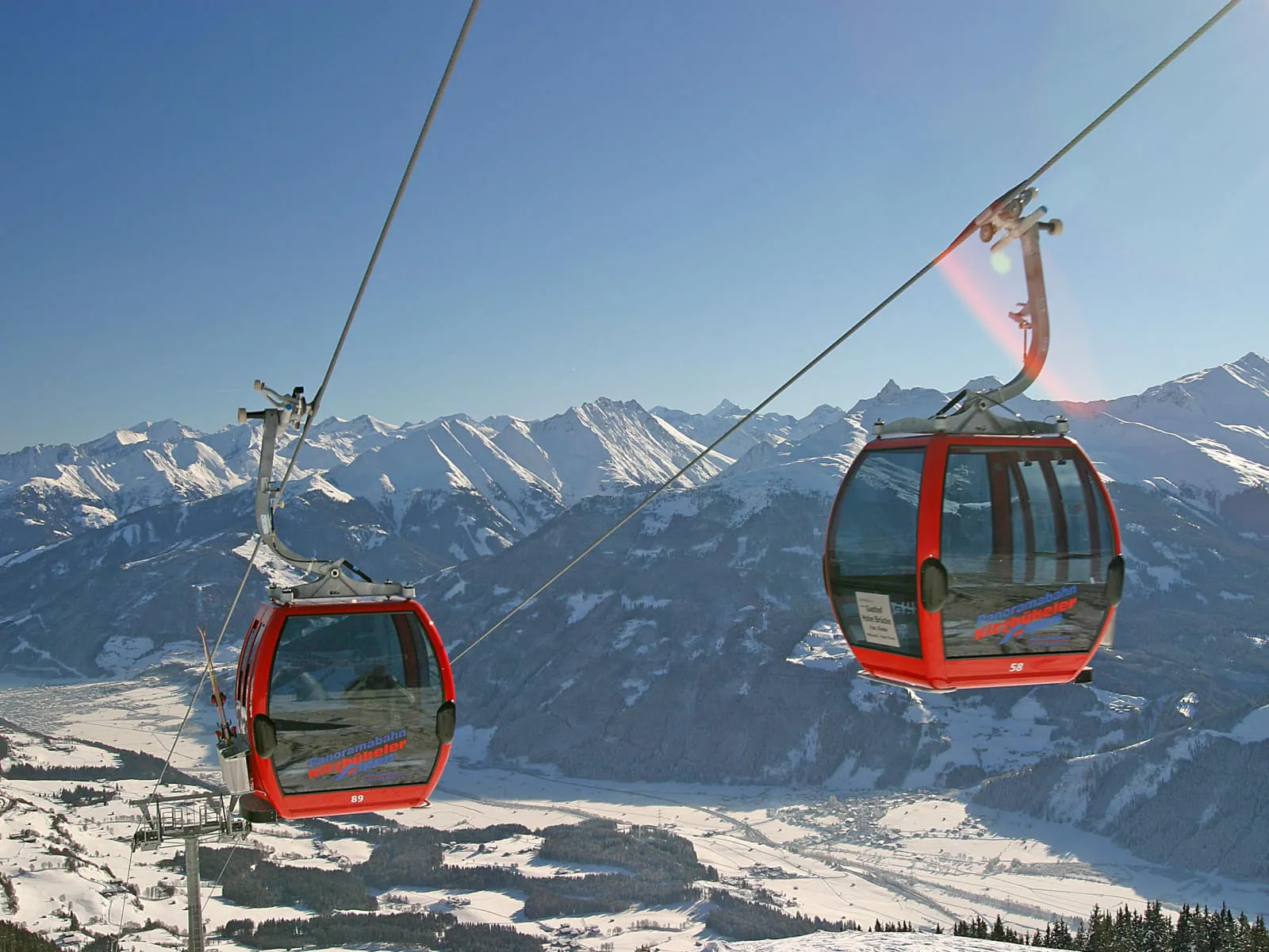 Zwei rote Gondeln der Seilbahn über schneebedeckte Berge und ein Tal