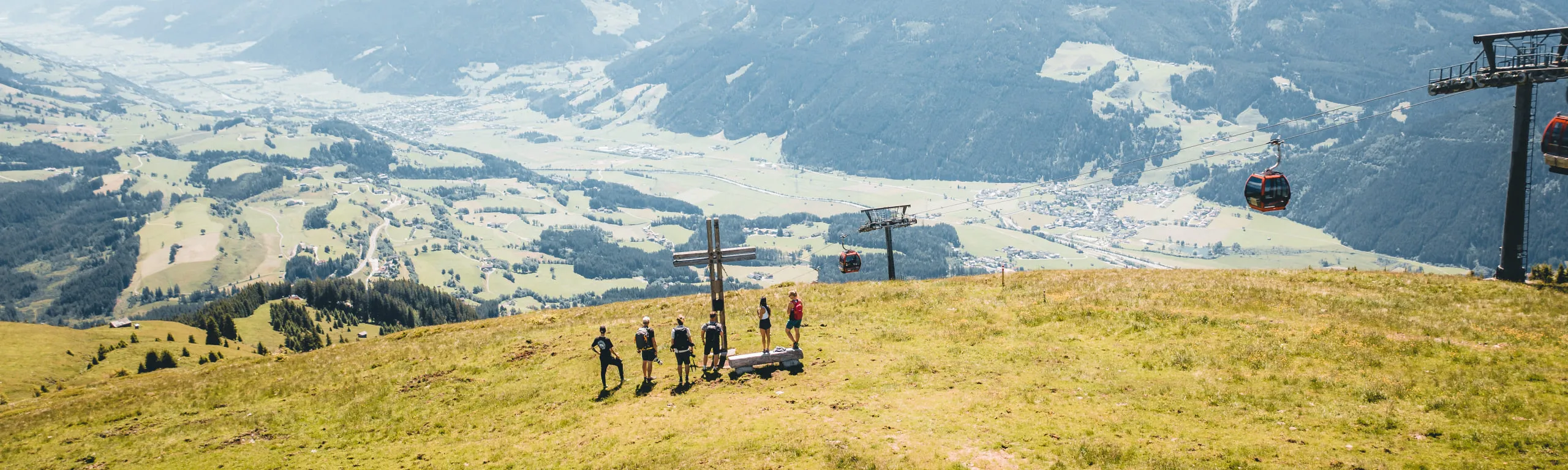 Gruppen von Menschen auf einer Wiese mit Seilbahn im Hintergrund und Blick ins Tal