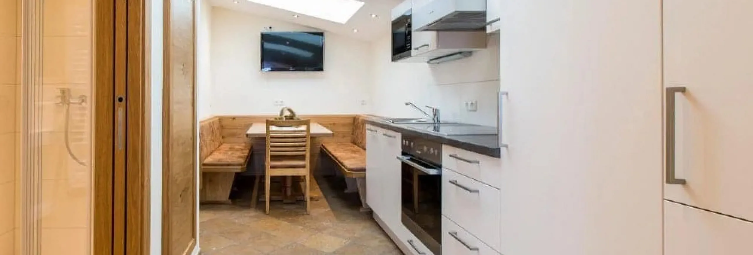 Moderne Küche mit Esstisch und Fernseher im Hintergrund